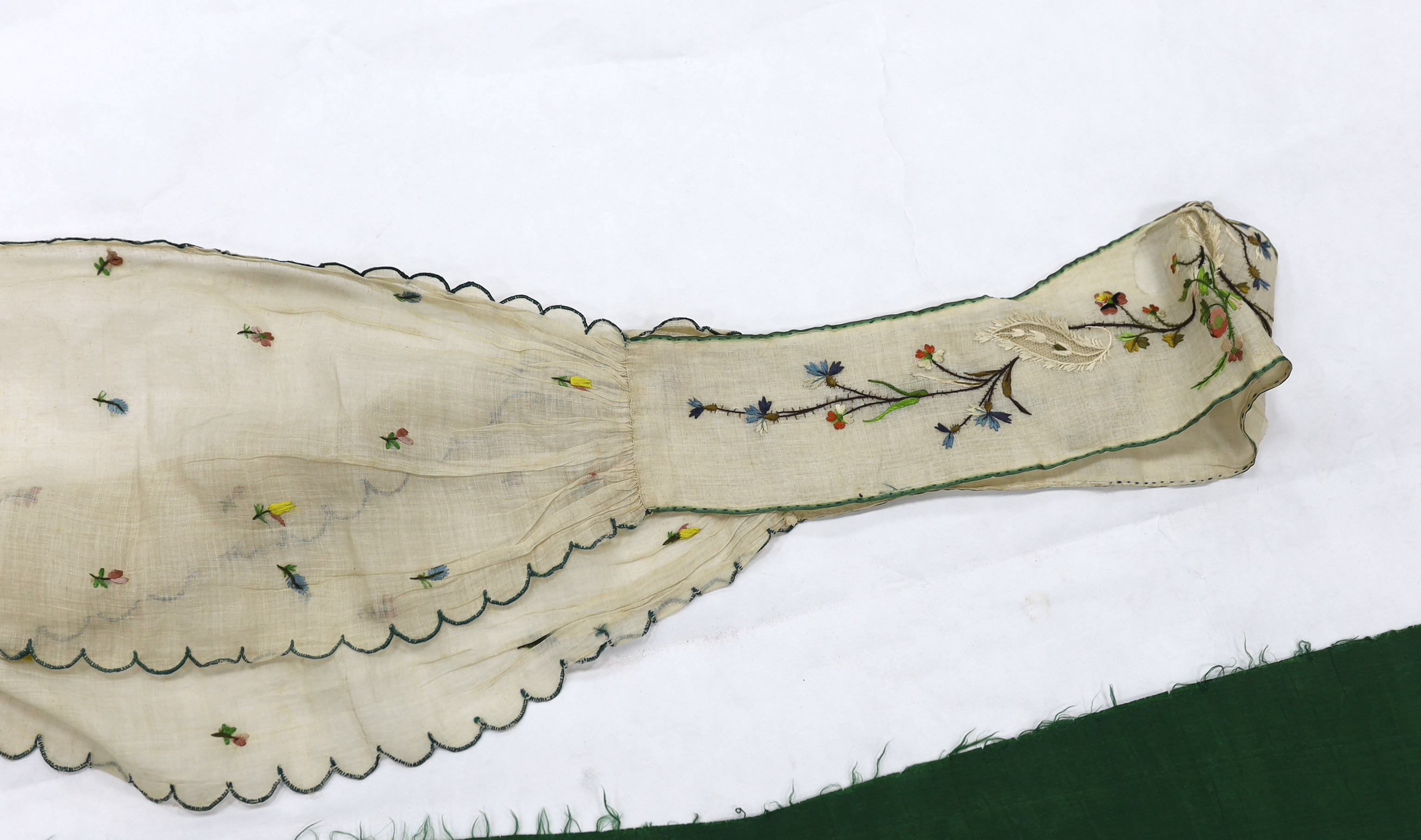 A late 18th century green silk scalloped bordered lady’s apron border, ornately embroidered with gold metallic threads and polychrome silk, in a large vine, floral and leaf design, together with a similar cream silk embr